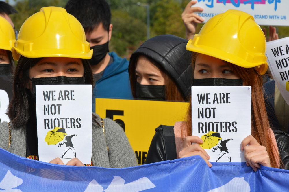Protesters in yellow helmets hold 'we are not rioters' signs, in solidarity with Hong Kong