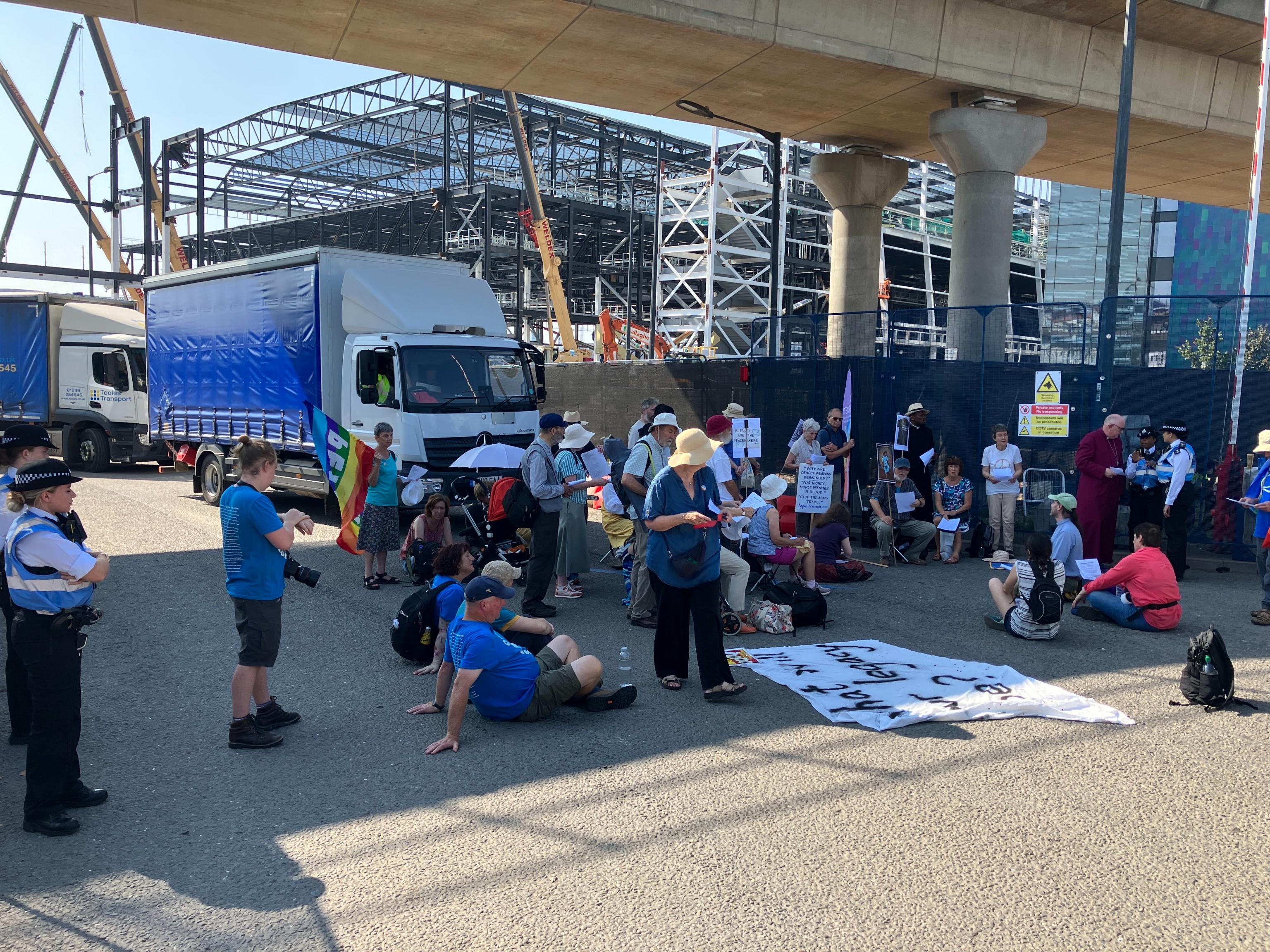 Protesters sitting in road under bridge as arms trade trucks wait going nowhere
