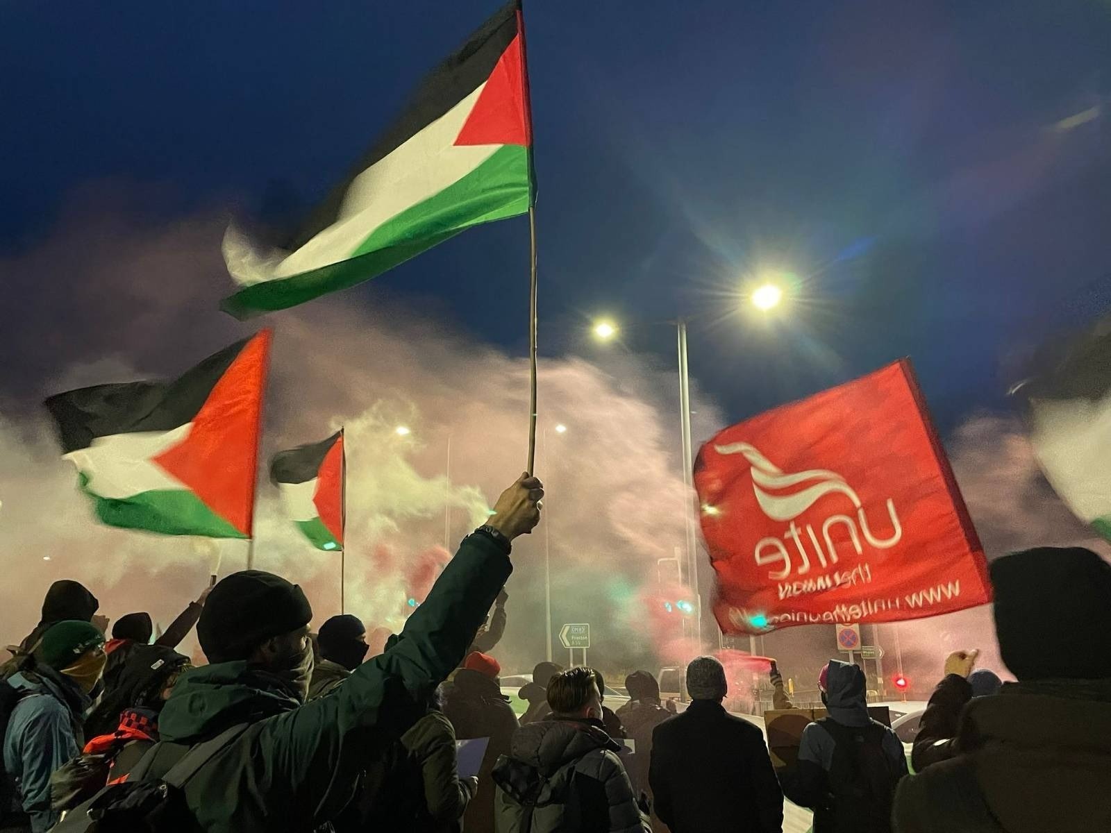 Unite banner and Palestine Solidarity banners amid smioke outside BAE Systems Samlesbury