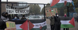 Image of a small protest blocking the gates of an arms factory.