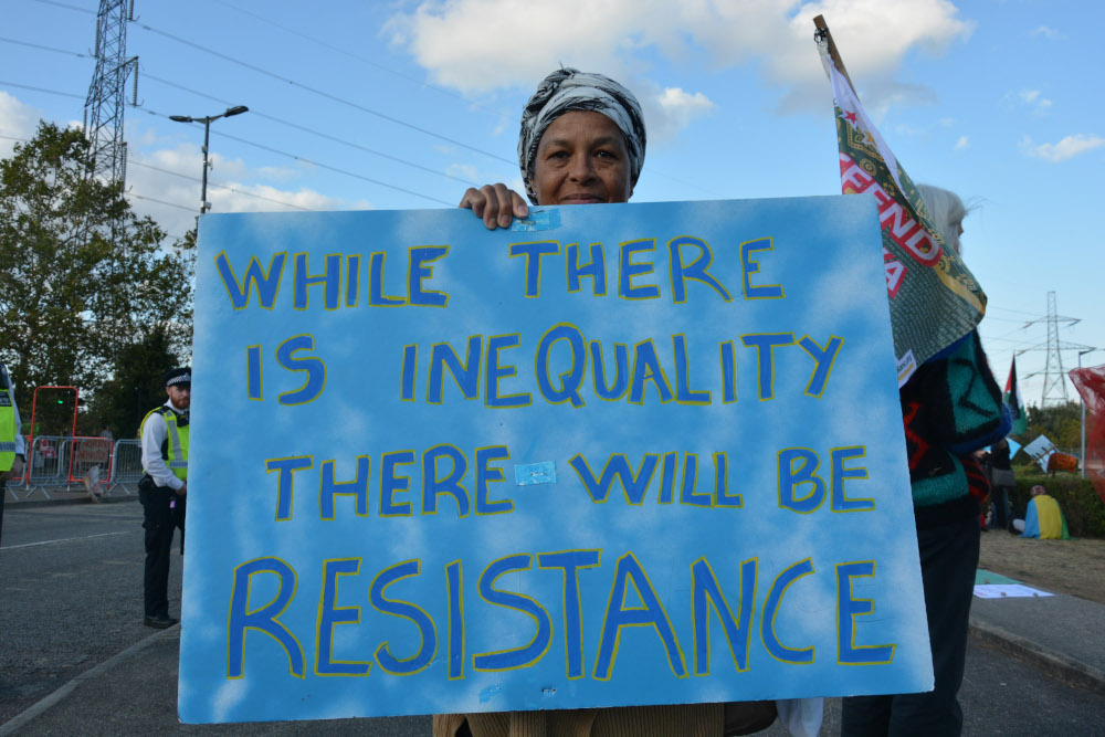 Person holds big placard saying Where there is inequality there will be resistance